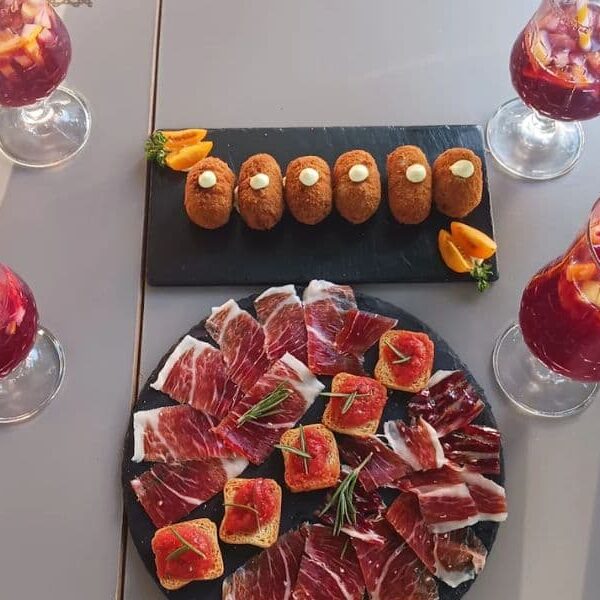 mesa con plato de jamon y plato de croquetas y vasos con tinto de verano